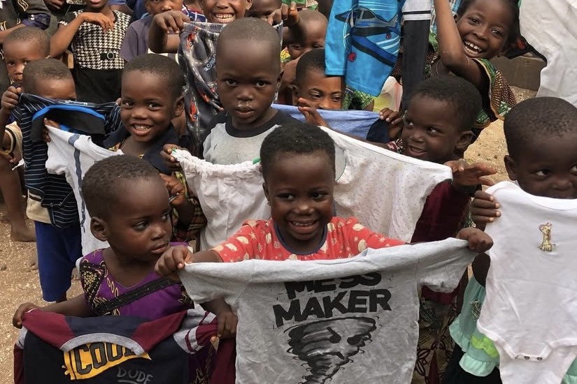 Smiling children holding up donated clothes at a community distribution in Lagos